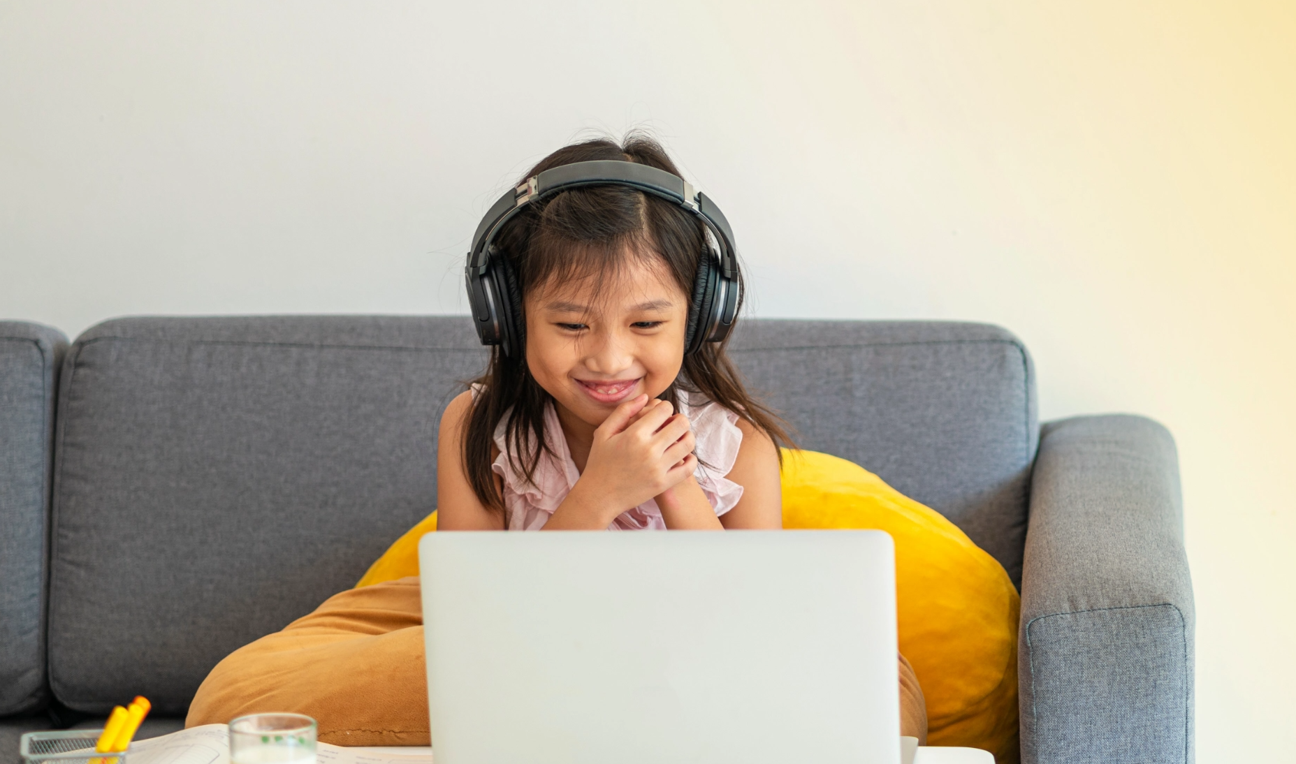 Young girl wearing headphones and using library online services smiles at a laptop screen.